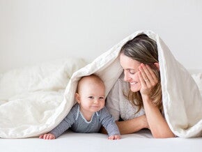 A mother with her baby under the sheets to enjoy motherhood.
