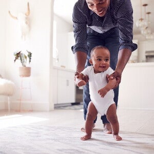 Baby’s first steps are an important part of his development A toddler taking his baby first steps with his father’s help.