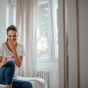 The first trimester is an important part of the development of a baby. A woman smiling at a pregnancy test in the early first trimester.