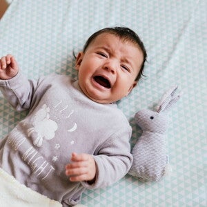 Learn how to understand why babies cry with this guide. A baby crying inside their crib.