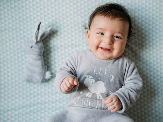 A toddler smiling in bed without any baby’s tummy problems