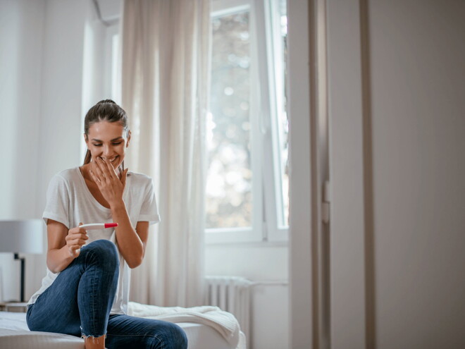 A woman smiling at a pregnancy test in the early first trimester.