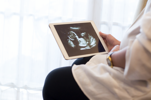 Pregnant woman watching ultrasound image on a digital tablet.