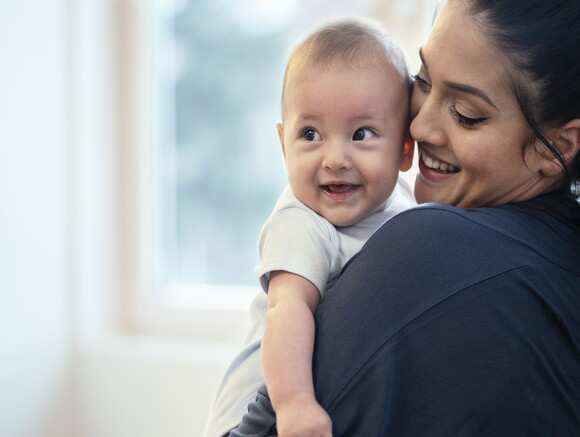 A woman holding her baby while they smile.