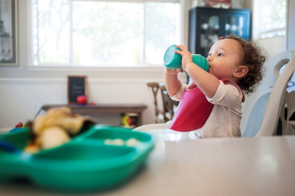 Hydration is important for a heathy toddler diet. A baby drinking water while sitting in highchair at home.