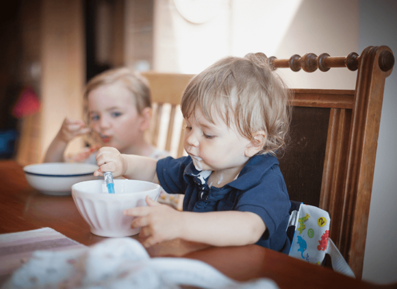 Two toddlers eating together at home.